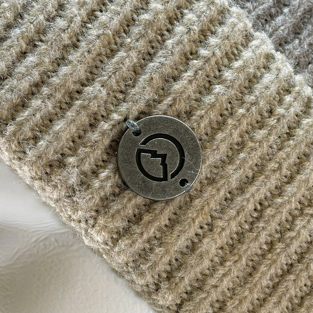 Close up of medallion on Domex Soft pink and taupe stripe cuffed beanie with a plush finish