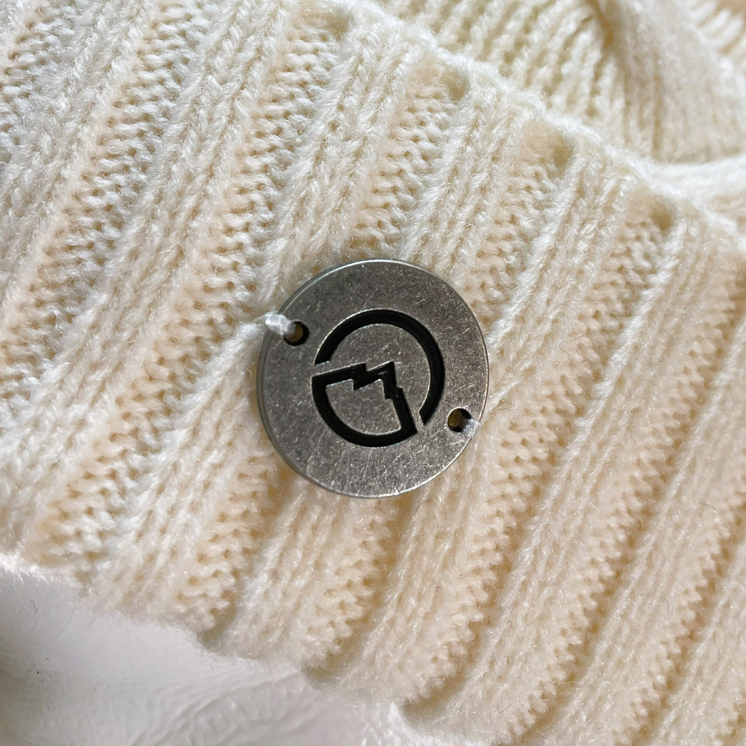 Close up of Domex medallion on White thick cable knit cuffed beanie 