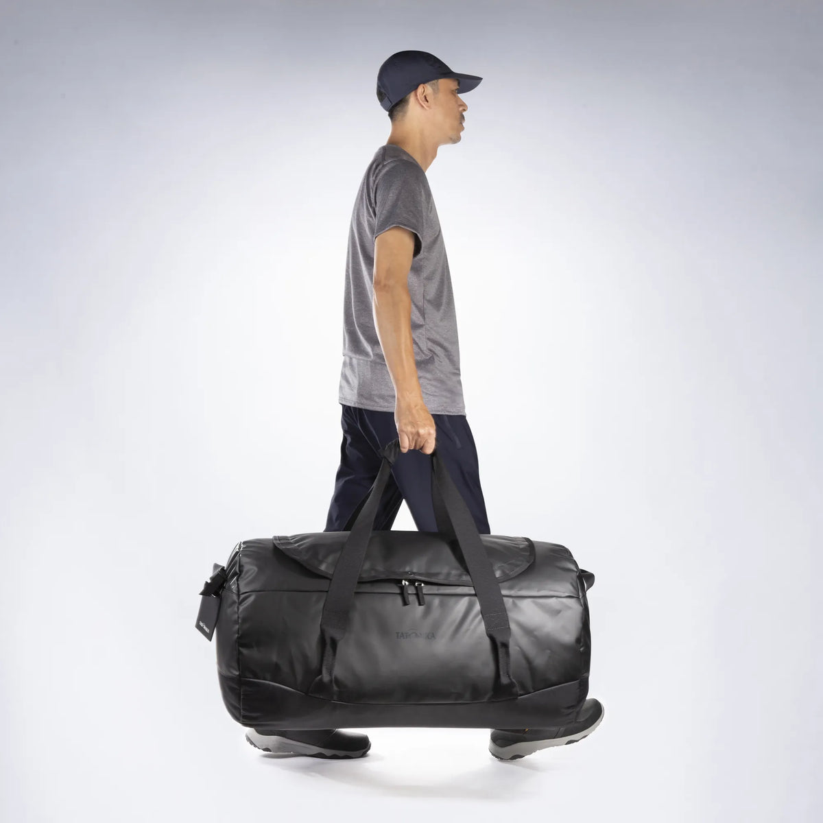 Being carried by the handles of the Tatonka Basic Barrel 85 L in matte black | TADI.6982.408